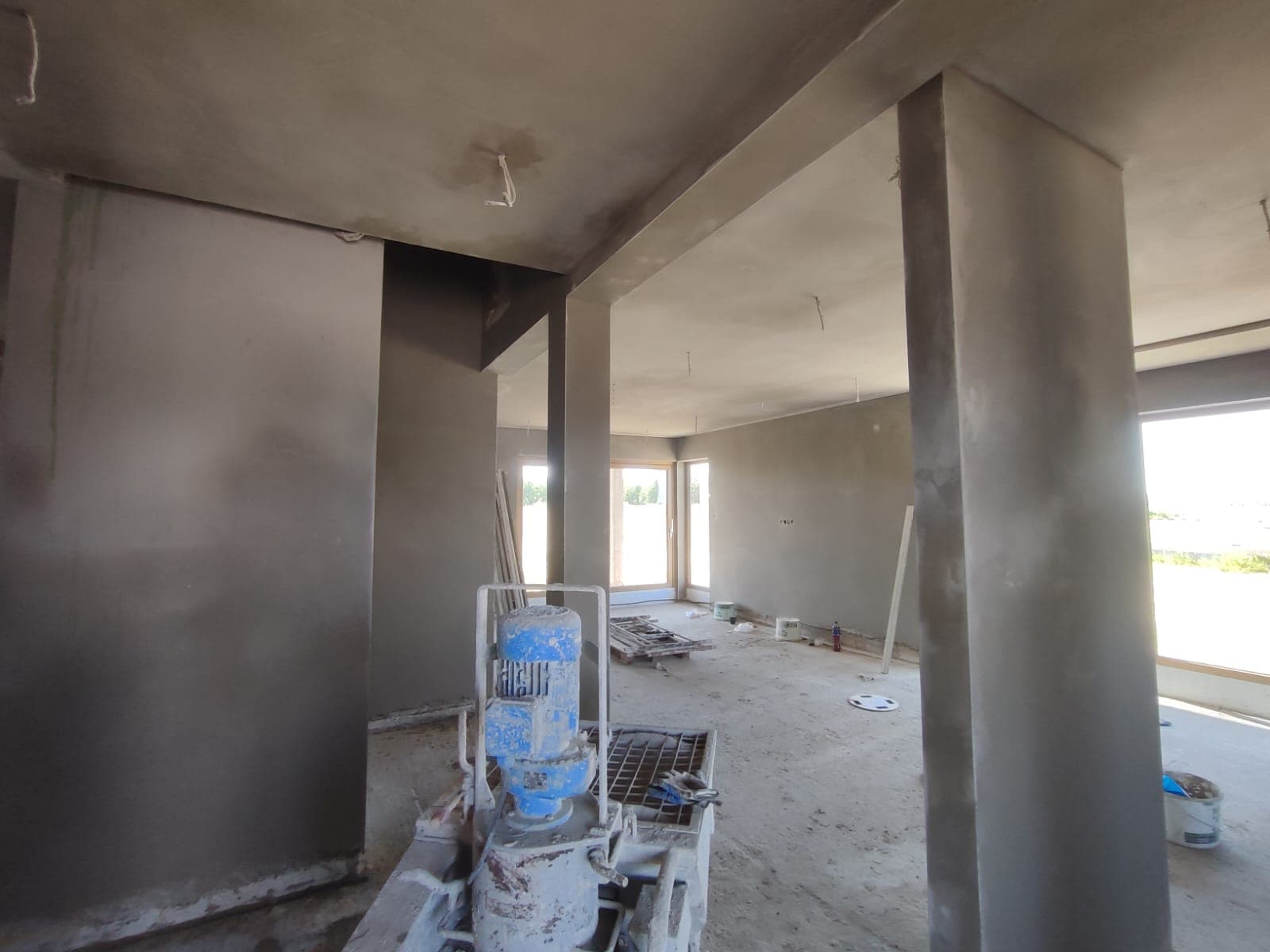 Tynki cementowe w salonie z filarami i maszyną tynkarską
